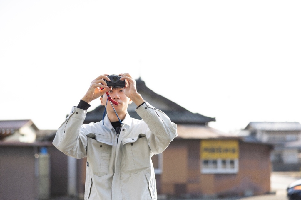 現場でコンパクトデジタルカメラを構え、記録写真を撮影する作業員