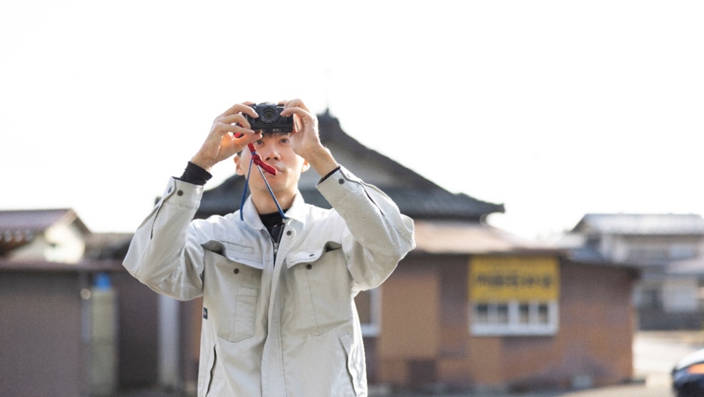 現場でコンパクトデジタルカメラを構え、記録写真を撮影する作業員