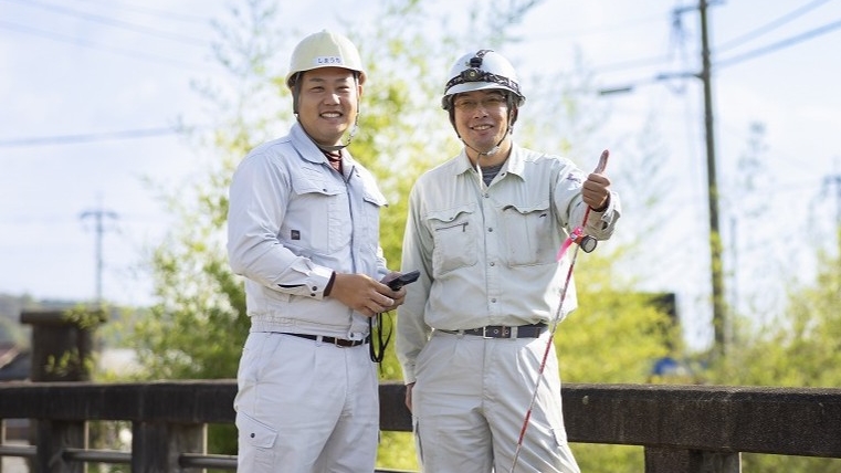 橋の上でサムズアップをして笑顔を見せる2名の作業員