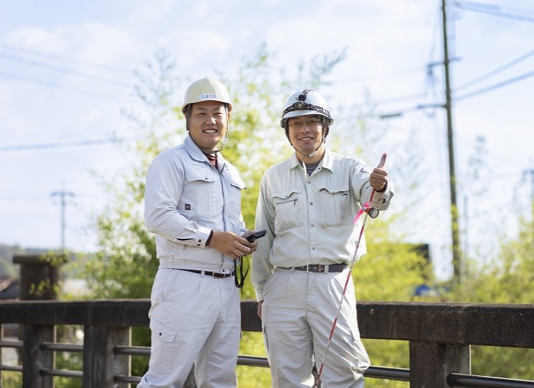 橋の上でサムズアップをして笑顔を見せる2名の作業員