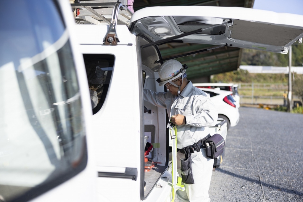 社用車のハッチを開け、安全ベストなどの装備を準備する時尾さん
