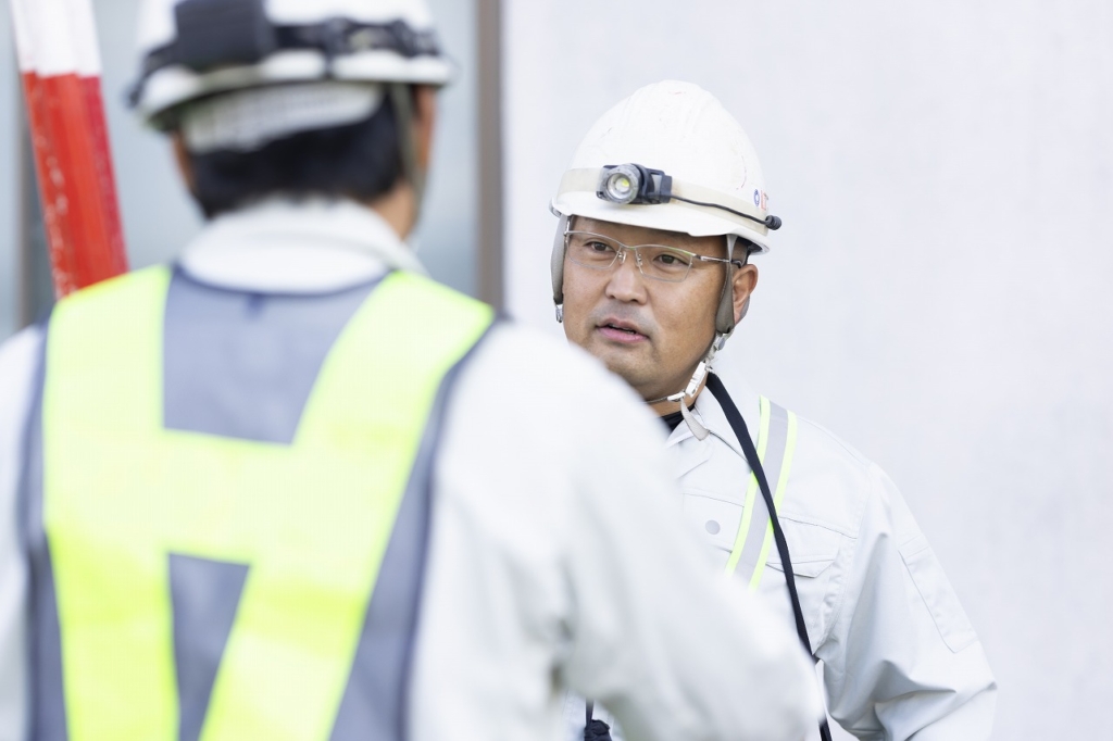 ヘルメットとメガネを着用し、現場で話をしている時尾さん