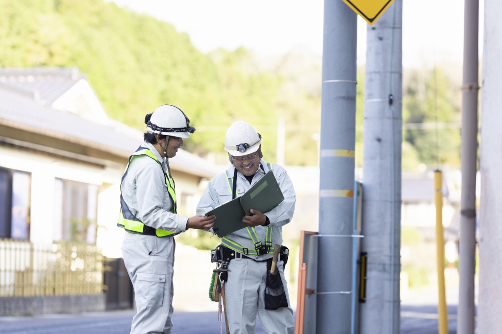 屋外でバインダーの資料を指差し、打ち合わせをする2名の作業員