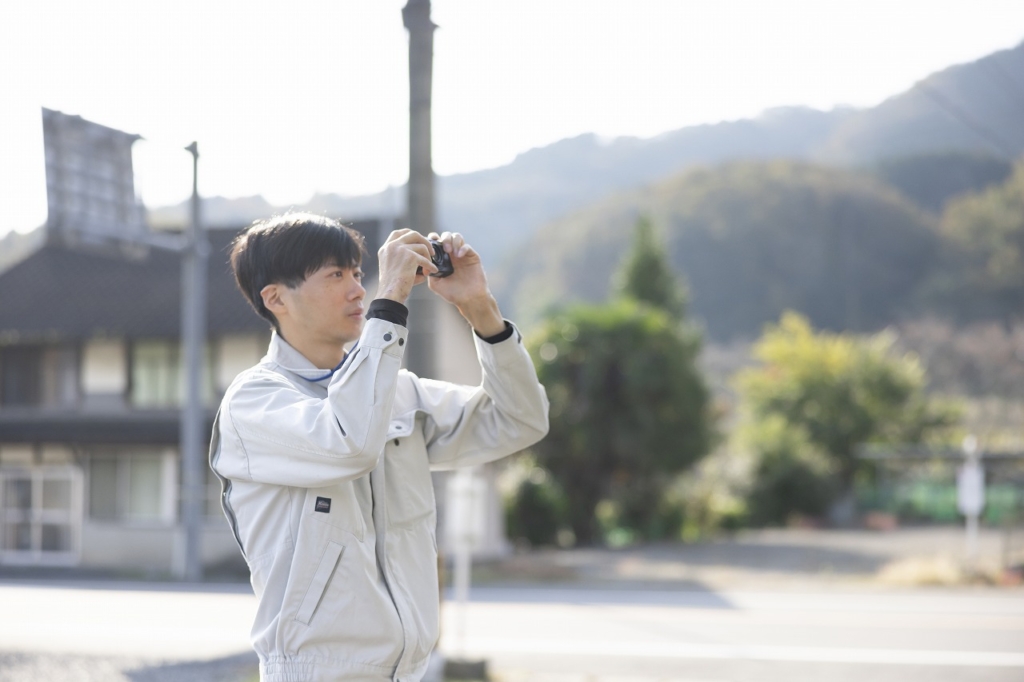 現場でコンパクトデジタルカメラを構え、記録写真を撮影する作業員