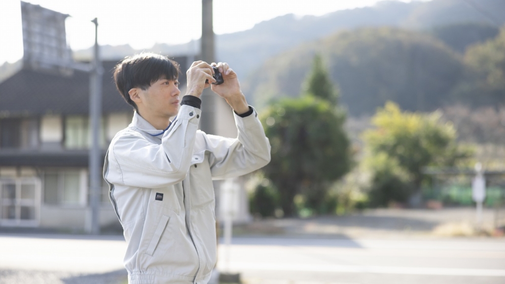 現場でコンパクトデジタルカメラを構え、記録写真を撮影する作業員