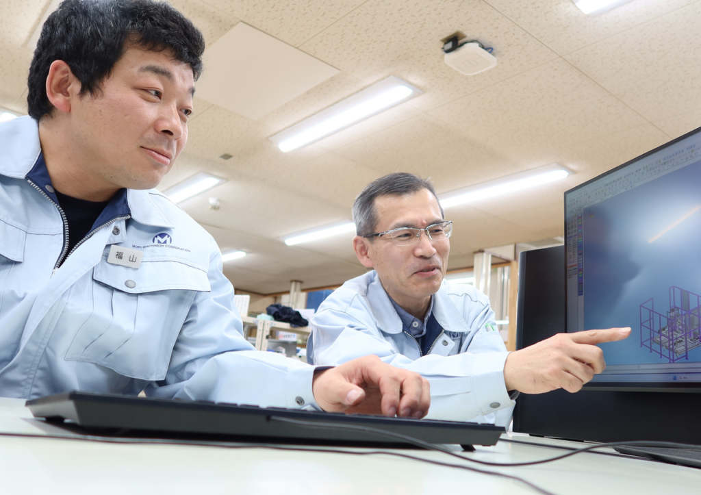 先輩社員と一緒にパソコンのモニターを見て、話をしている福山さん