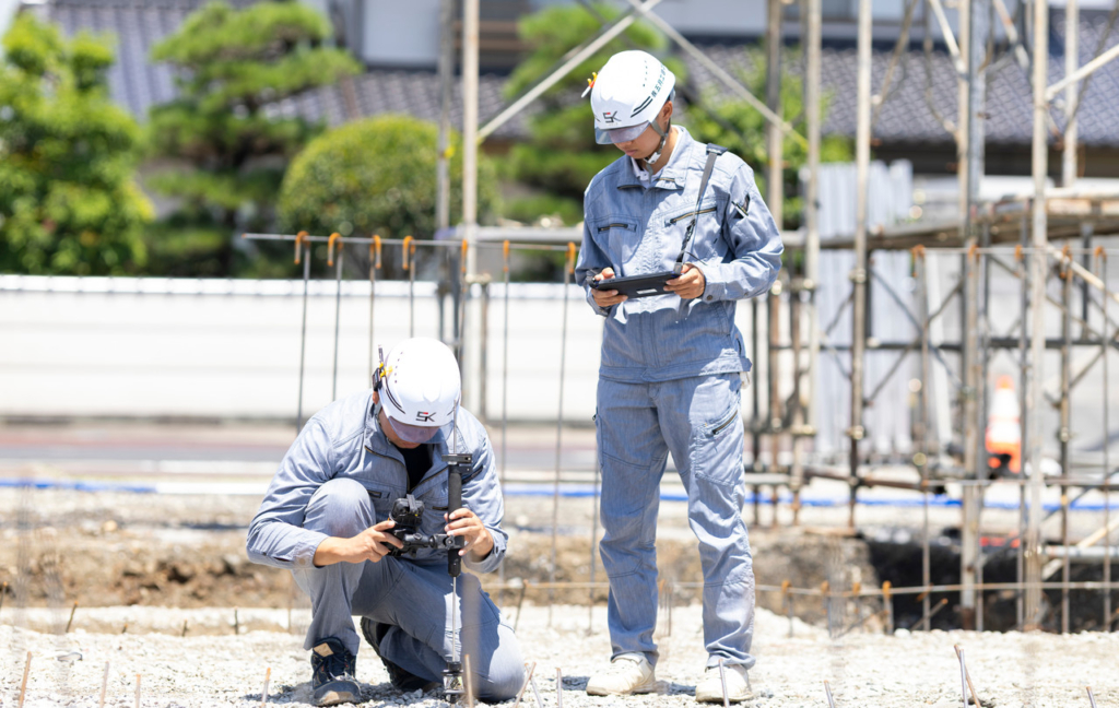 建設現場で、タブレット端末や計測機器を用いて同僚と作業をしている明石さん