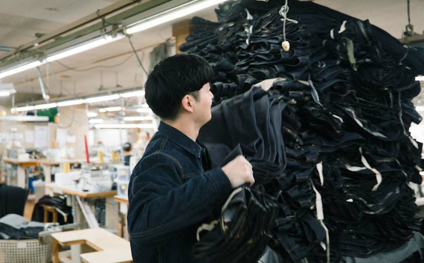 工場内で、デニムジーンズの束を抱えている内田さん