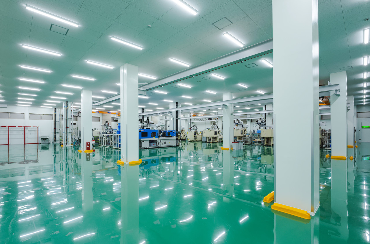 緑色の床が広がり、整然と成形機などの設備が配置されている明るく清潔な工場内の風景