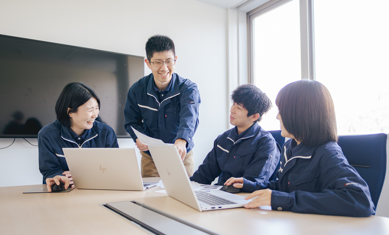 会議室でノートパソコンを前にし、談笑しながらコミュニケーションを取り合う4人の社員