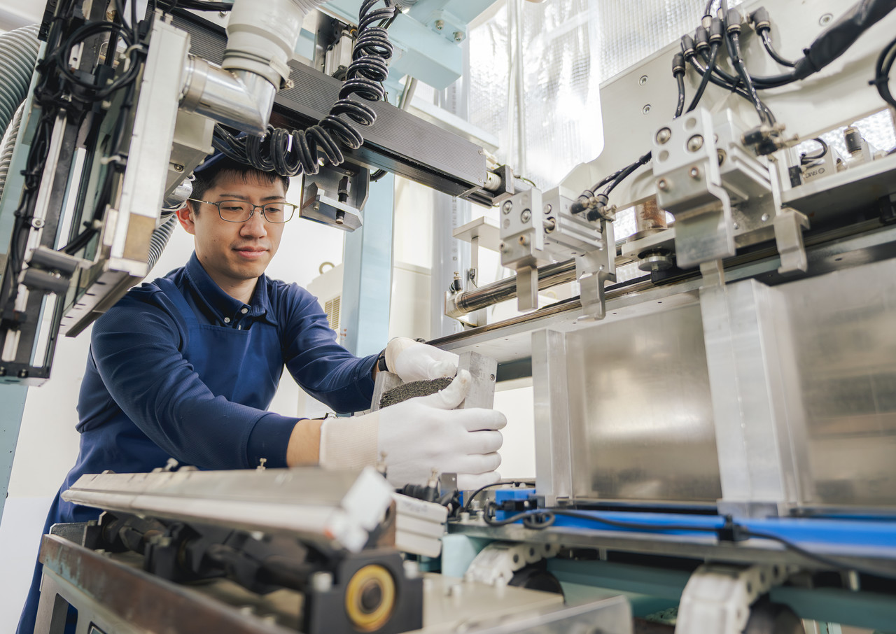 工場内で、機械の部品を両手で持ち、製造設備に設置している社員