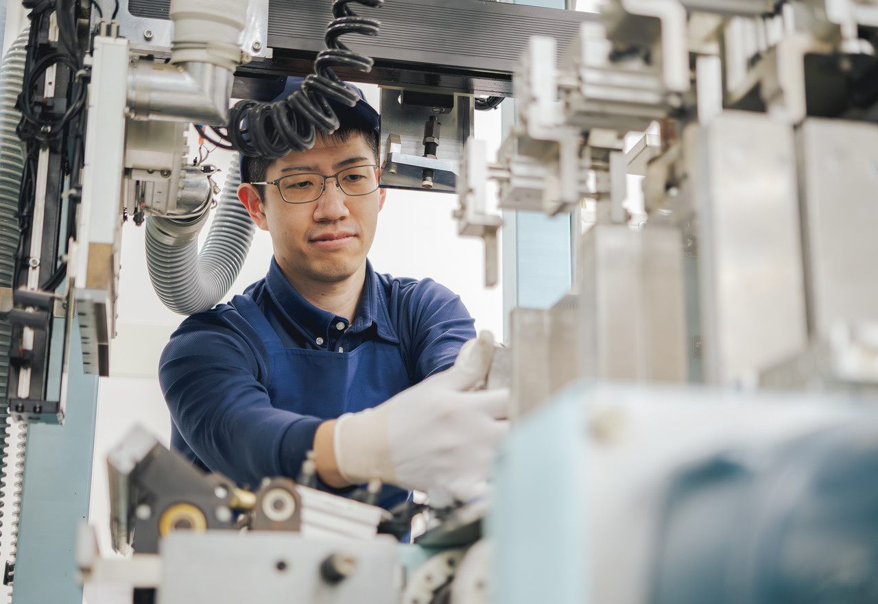 白い手袋をして、稼働している製造ラインの機械部分を調整している作業着姿の社員