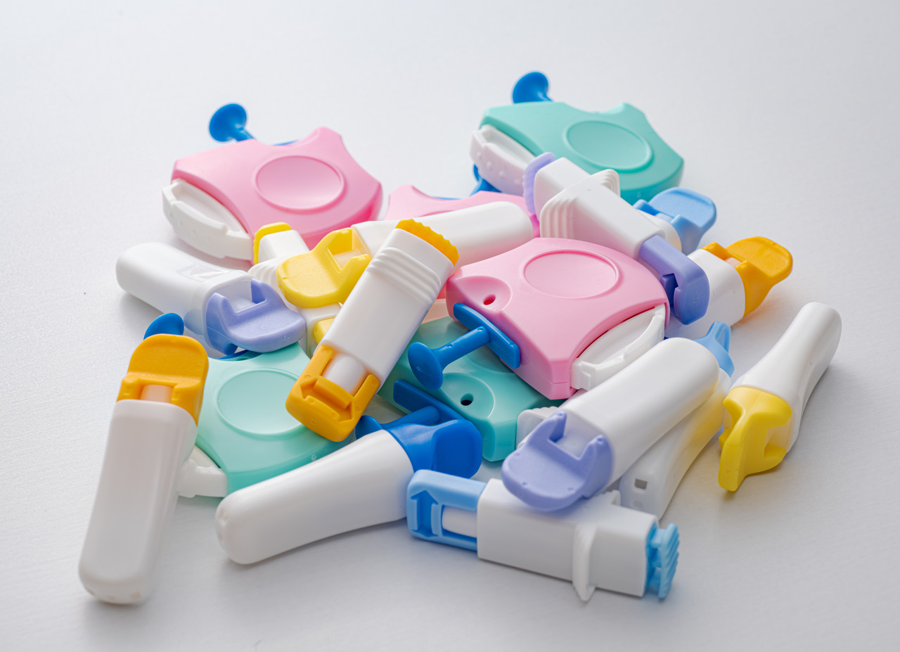 白い背景に山積みにされた、ピンクや水色など色とりどりの医療用採血器具ランセット