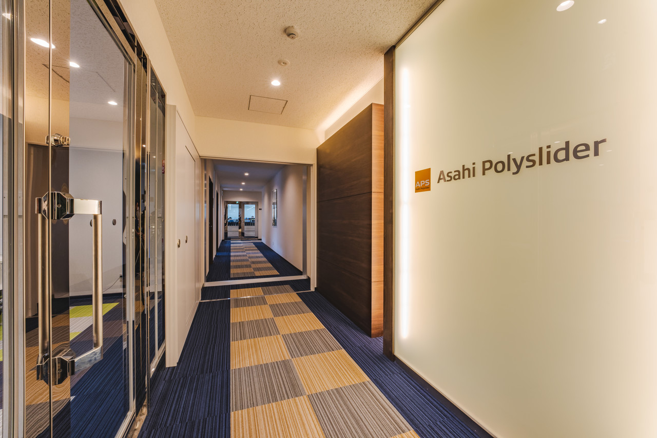 ガラス性のドアと、その向かいの壁に「Asahi Polyslider」のロゴがあり、奥へと続く社内の廊下