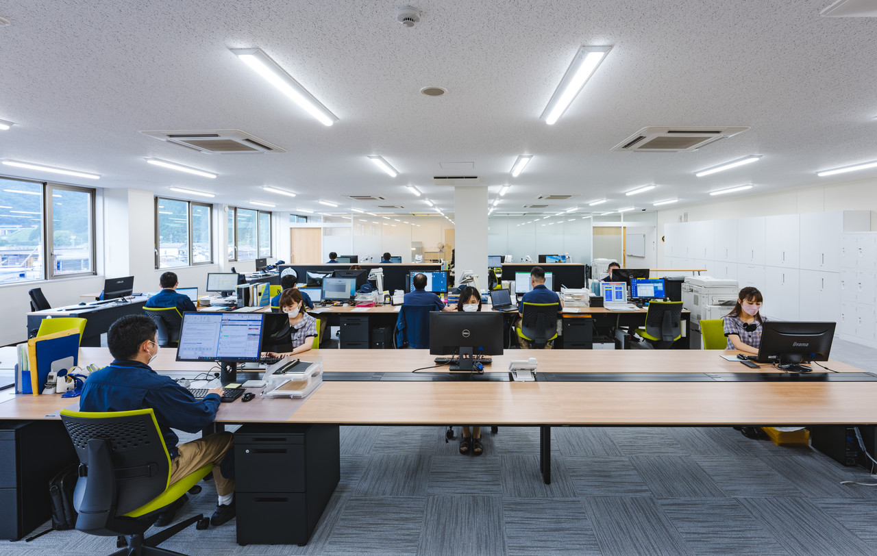 デスクが並ぶ明るく広々としたオフィス内で、パソコンに向かって作業をしている複数の社員