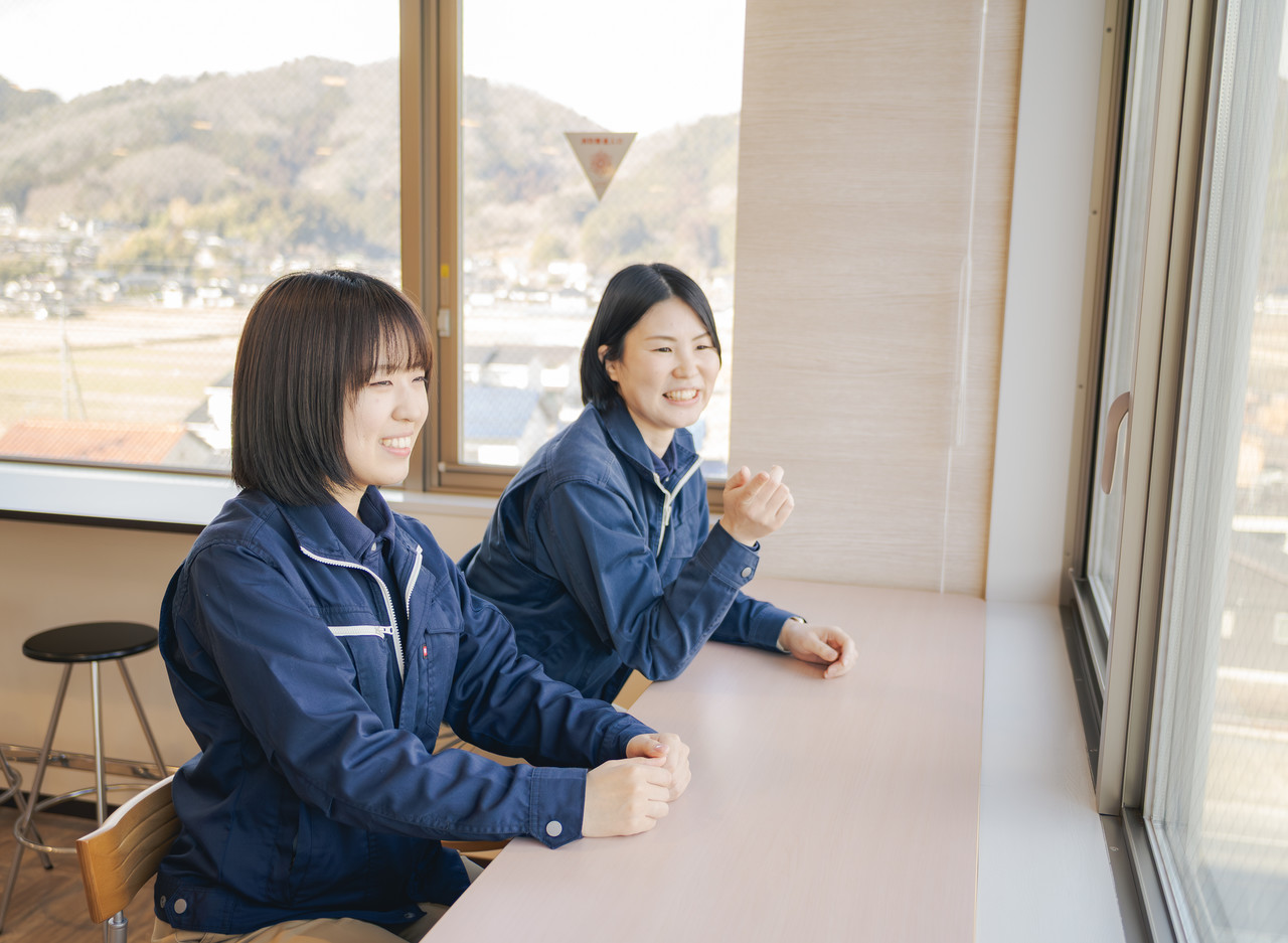共有スペースの窓際にあるカウンター席に並んで座り、外の景色を見ながら談笑する2人の女性社員
