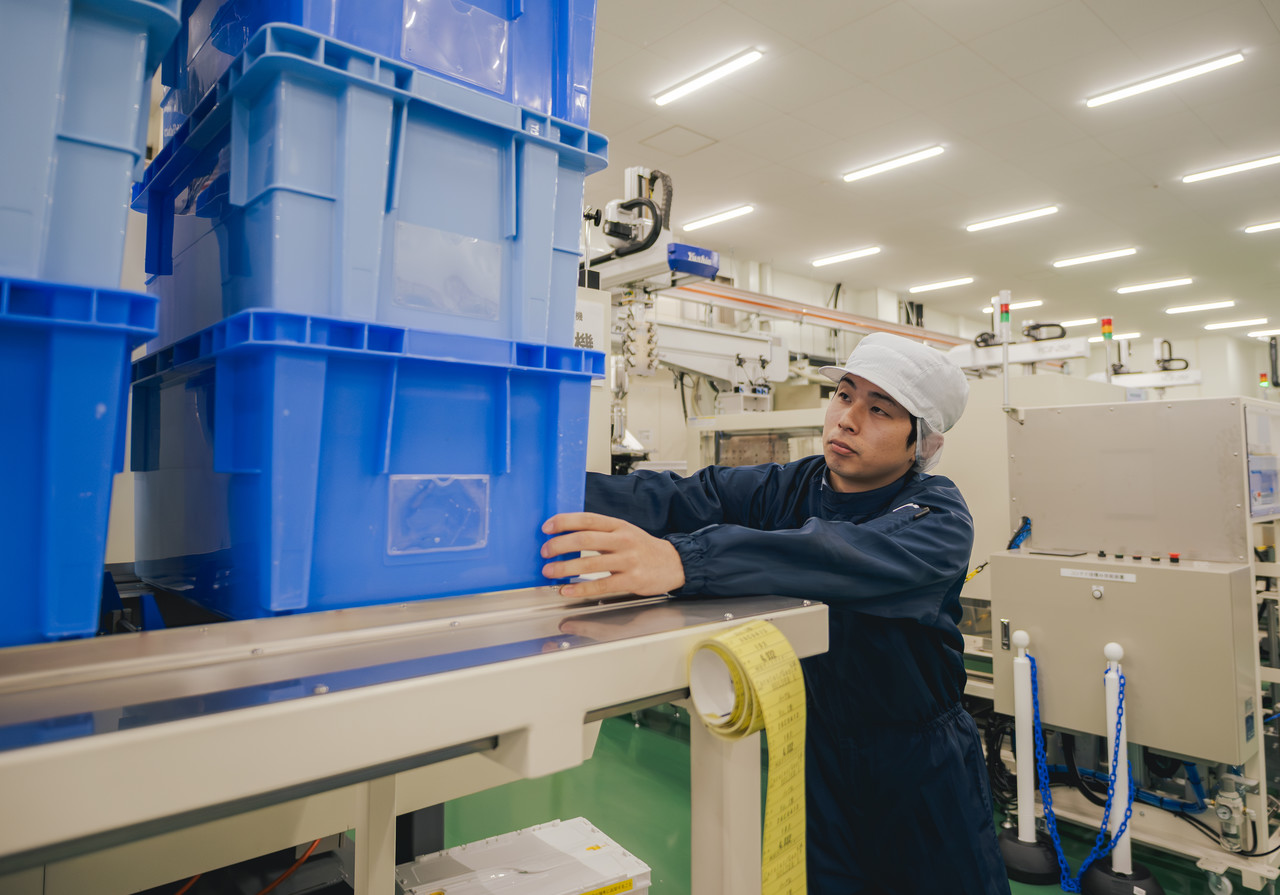 クリーンルーム内で、青いプラスチックコンテナを積み重ねて整理している庄司さん