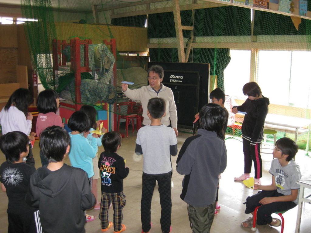 子どもたちに向けて紙ヒコーキの作り方を教える男性