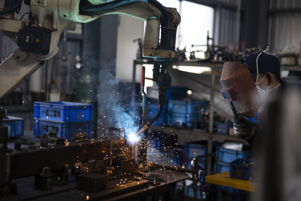 火花を散らしながら金属部品を溶接するロボットアーム