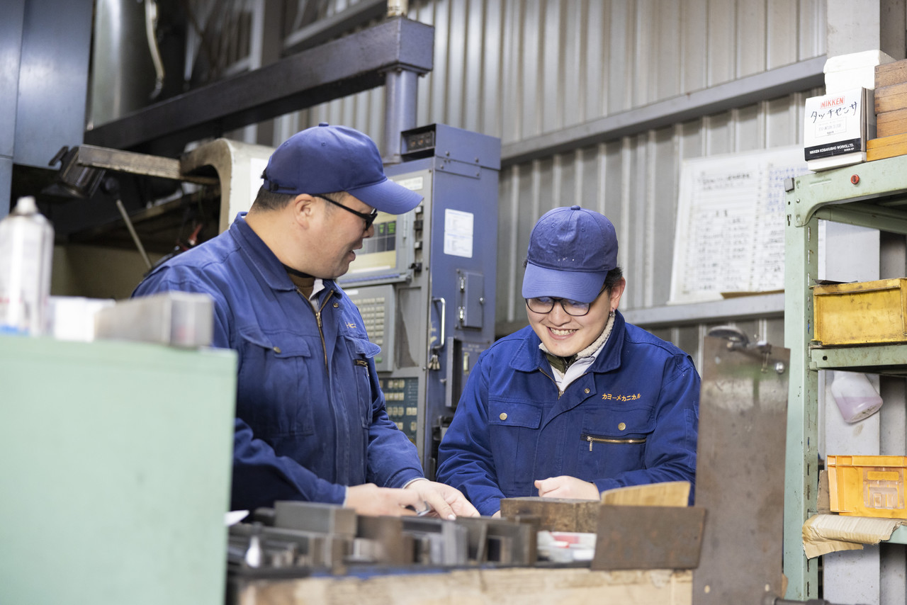 工場で作業をしながら笑顔で会話する2名の男性社員