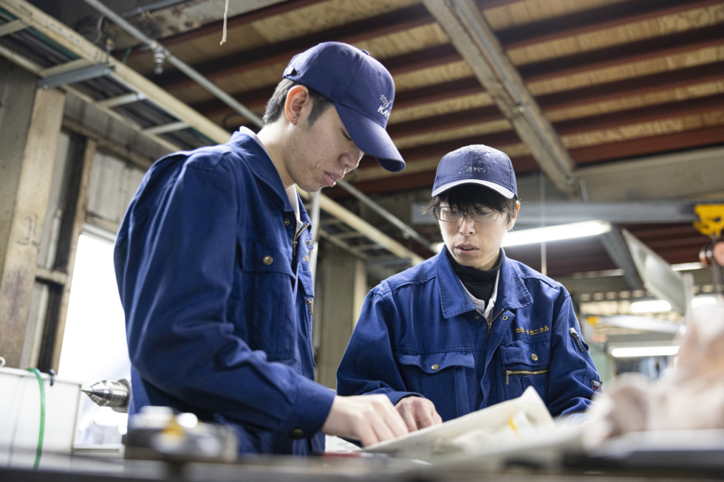 図面を確認しながら打ち合わせをする青い作業服の男性社員2名