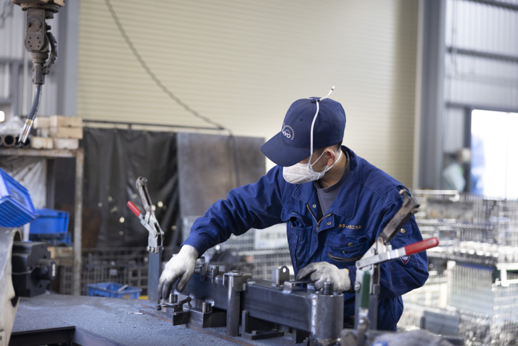 溶接ロボットの補助装置に部品をセットする作業員