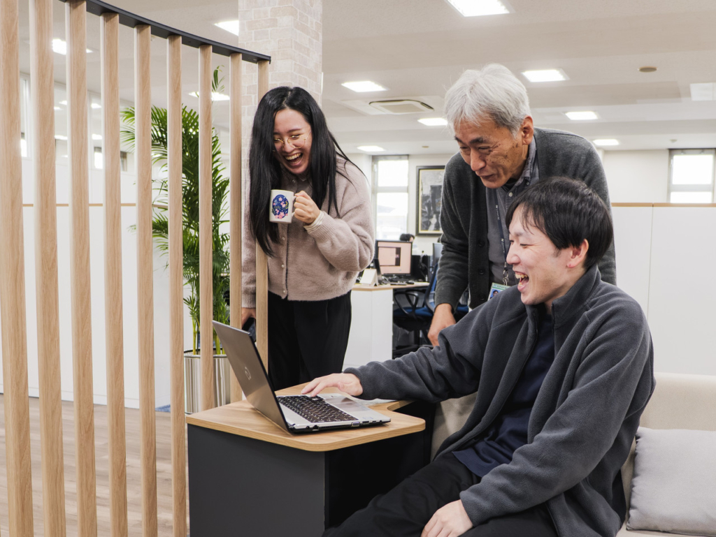 ノートパソコンを囲んで笑顔で会話する3名の社員