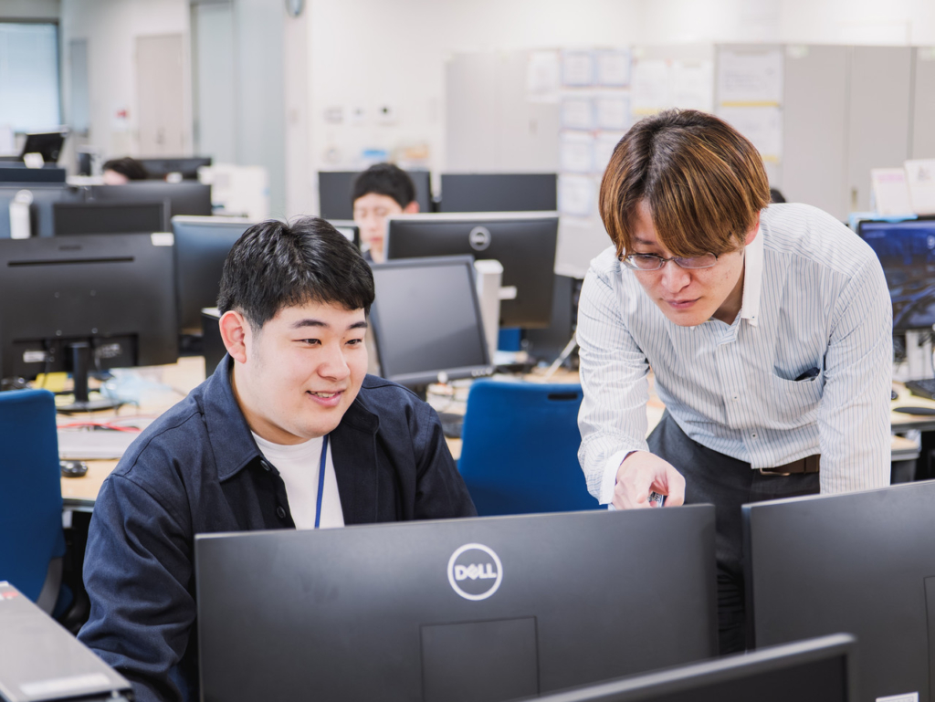 モニターを指差して確認し合う右手さんと男性社員