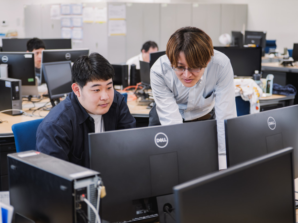 モニターを指差して確認し合う田中さんと男性社員