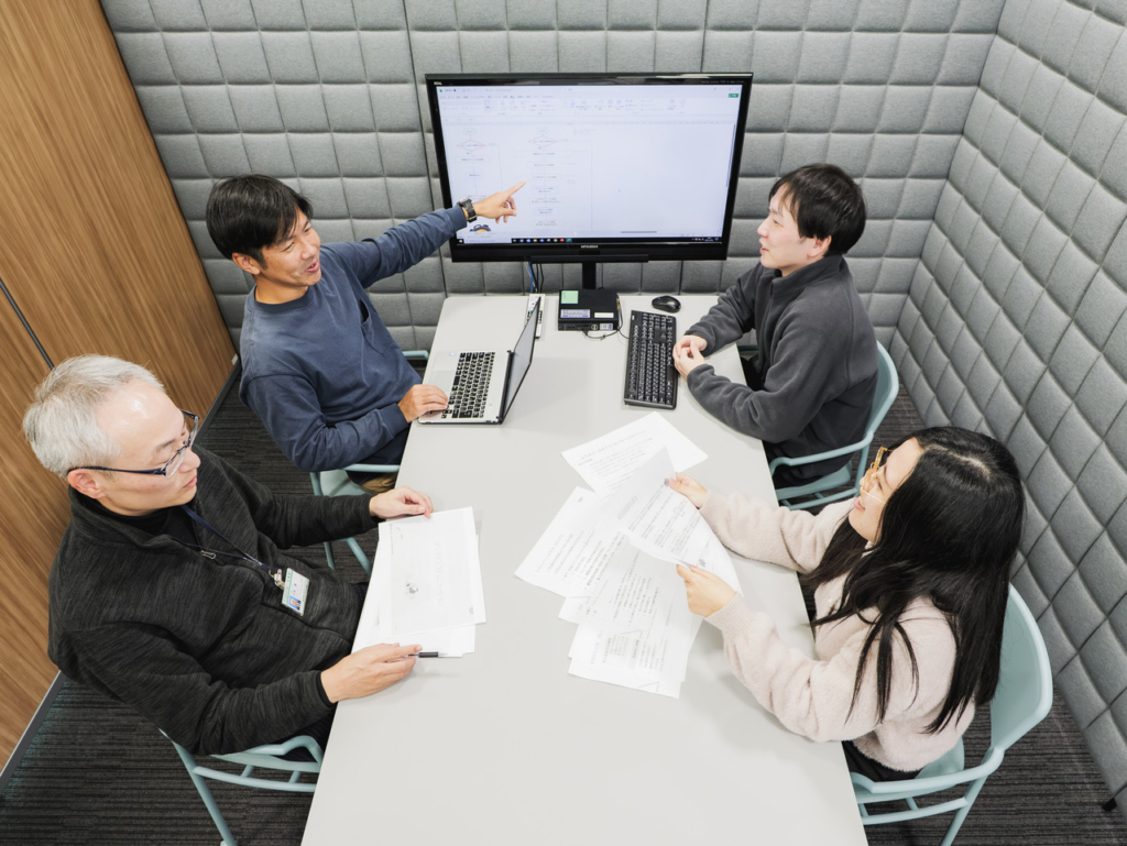 モニターに資料を映しながら打ち合わせをする4名の開発チーム