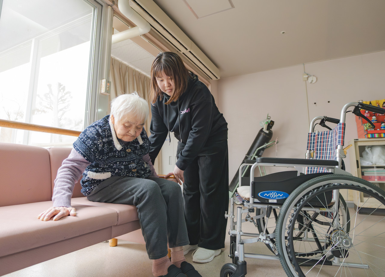 介護スタッフが利用者の力を活かしてベッドから車椅子へ移乗するサポートをしている様子