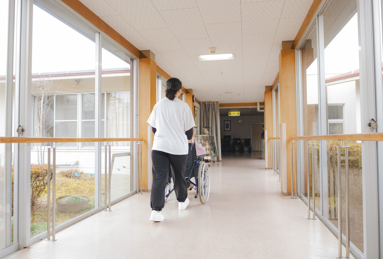 井上さんが、利用者の座った車椅子を押して施設内の廊下を歩いている様子