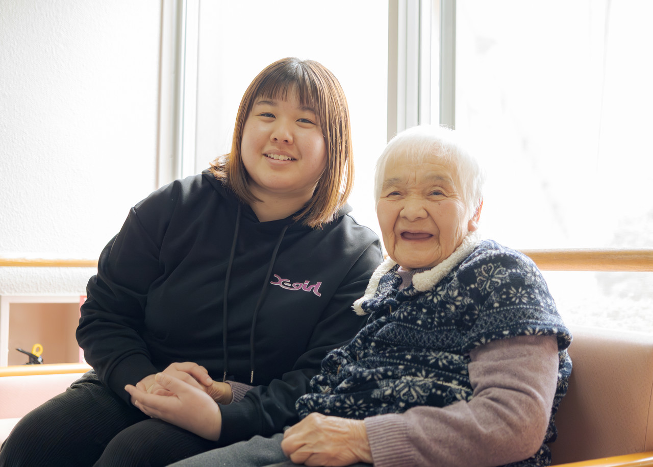 木原向葵さんと高齢の利用者が手を繋いで、2人でこちらを向いている様子