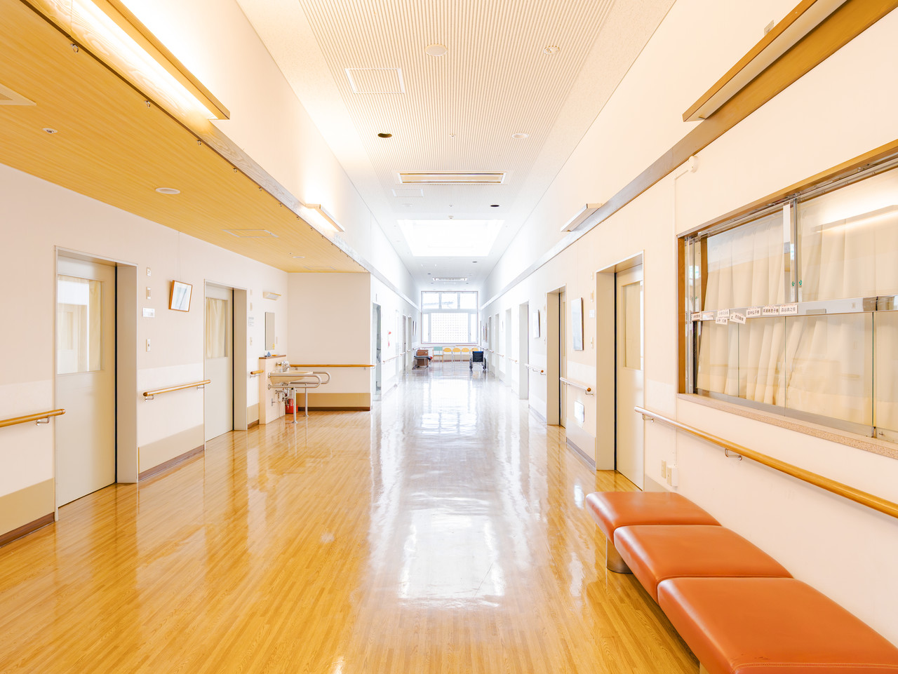 天窓からの自然光が差し込み、オレンジ色のベンチが置かれたショートステイエリアの廊下。