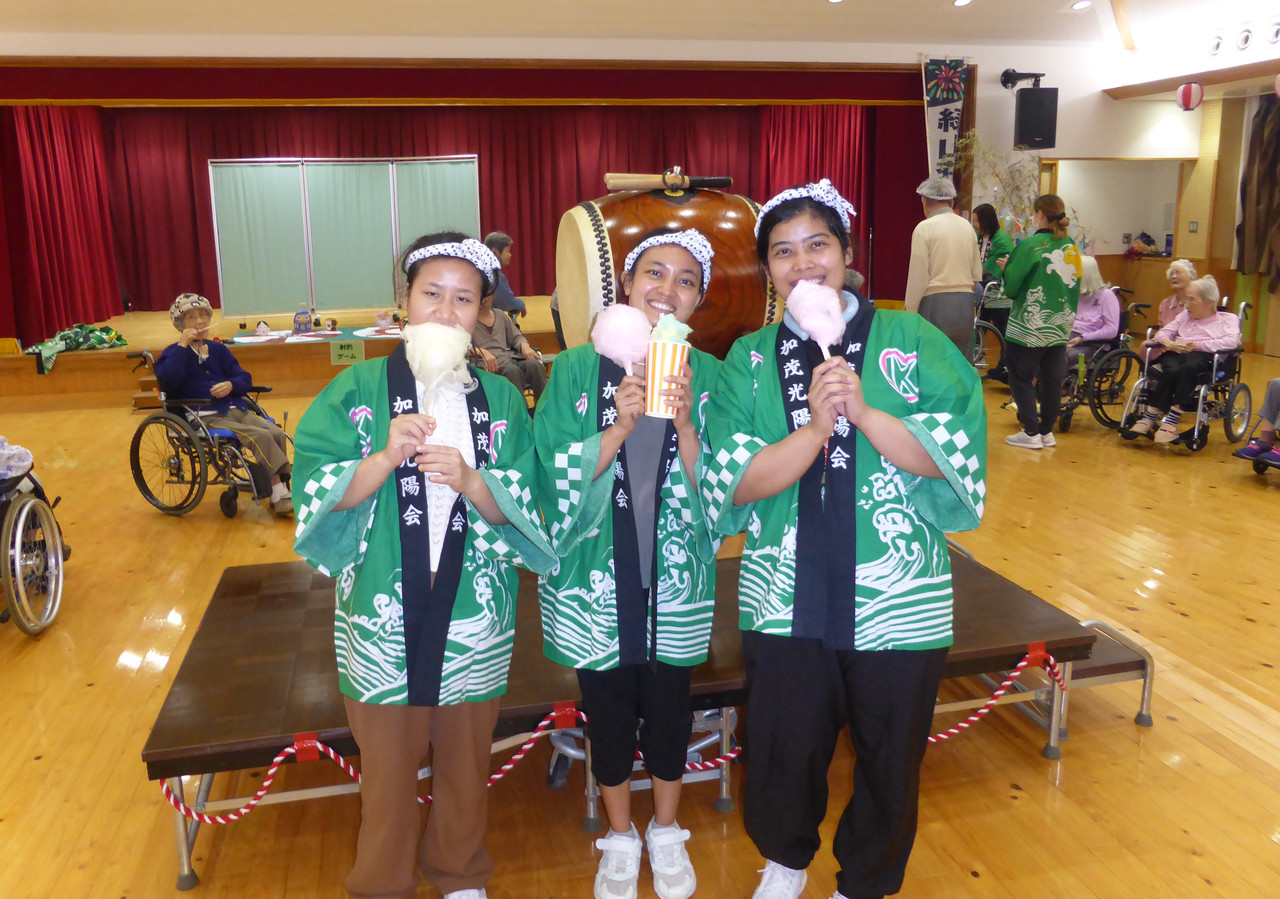 提灯が飾られた屋内の会場で、浴衣や法被を着た人たちが納涼祭の催し物を楽しむ様子