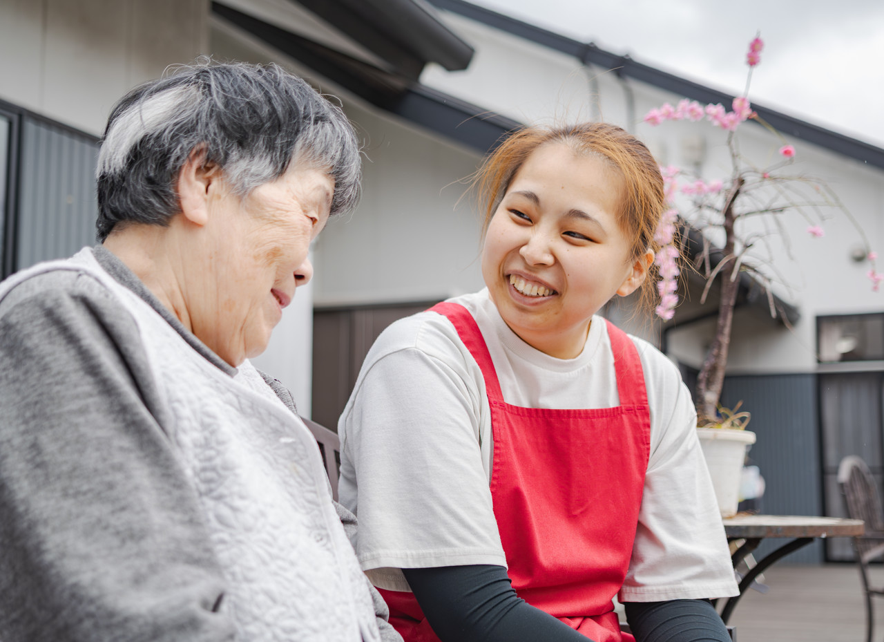 利用者と芳本さんがテラスの椅子に2人で座って談笑している様子