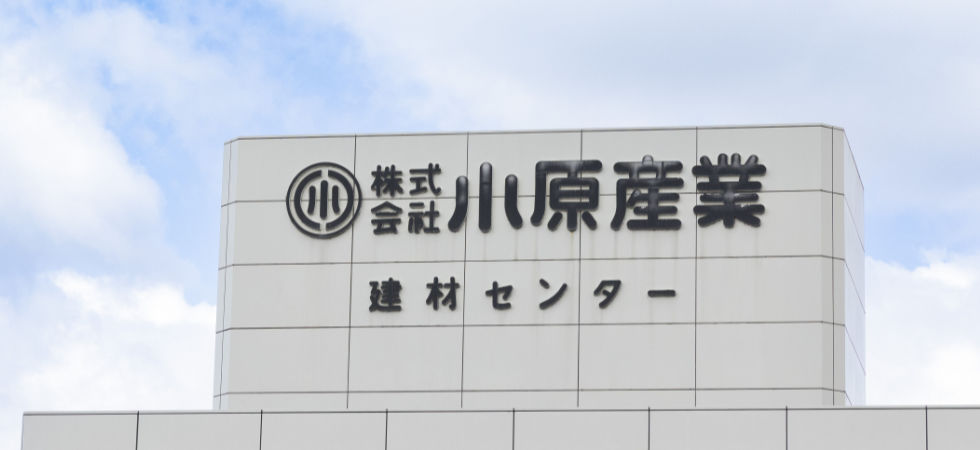 青空の下にある株式会社小原産業建材センターの白い建物の外観。