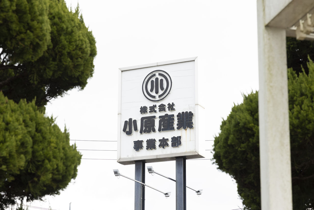 木々の間にある「株式会社小原産業 事業本部」と書かれた屋外看板