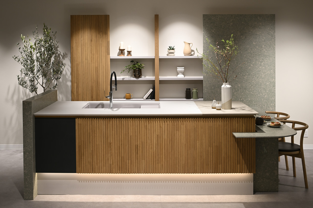 木目のパネルと白い天板が特徴的なキッチンカウンター。奥には木製の棚があり、植物や小物が飾られている。