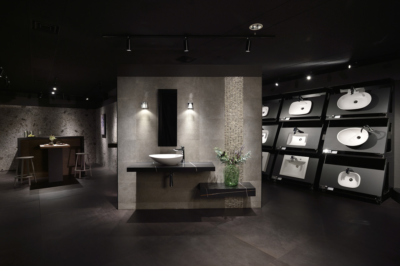 黒を基調とした薄暗いショールームの壁面に、様々な形状の白い洗面ボウルが展示されている様子。