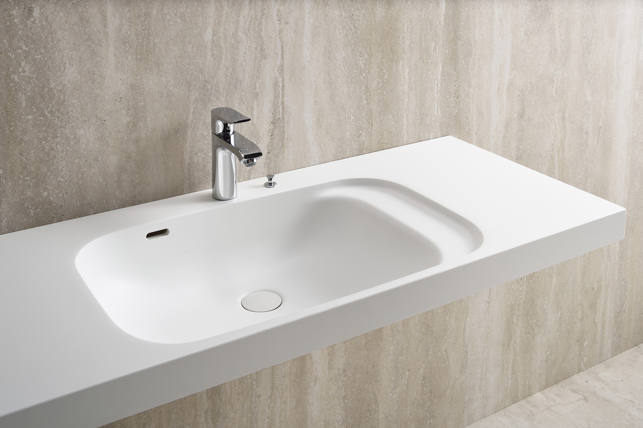 白い人工大理石で作られた洗面カウンター。シルバーの蛇口が設置されている。壁面はベージュの石目調。