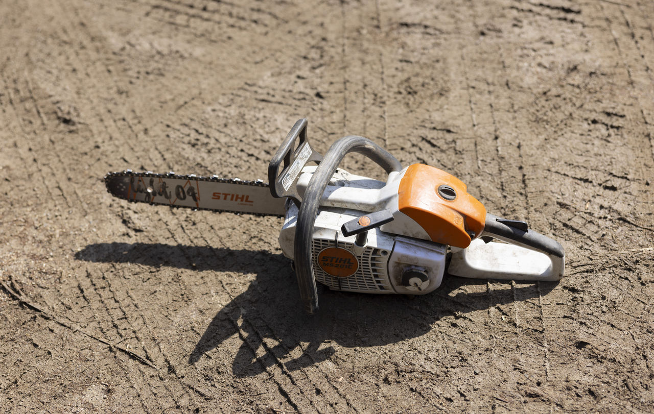 山林の地面に置かれたオレンジと白のチェーンソー
