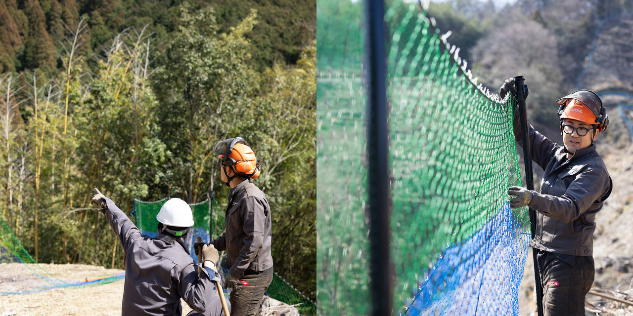 山の斜面で鹿よけネットの設置箇所を指差して確認する2人の作業員と、支柱にネットを取り付ける作業員の様子