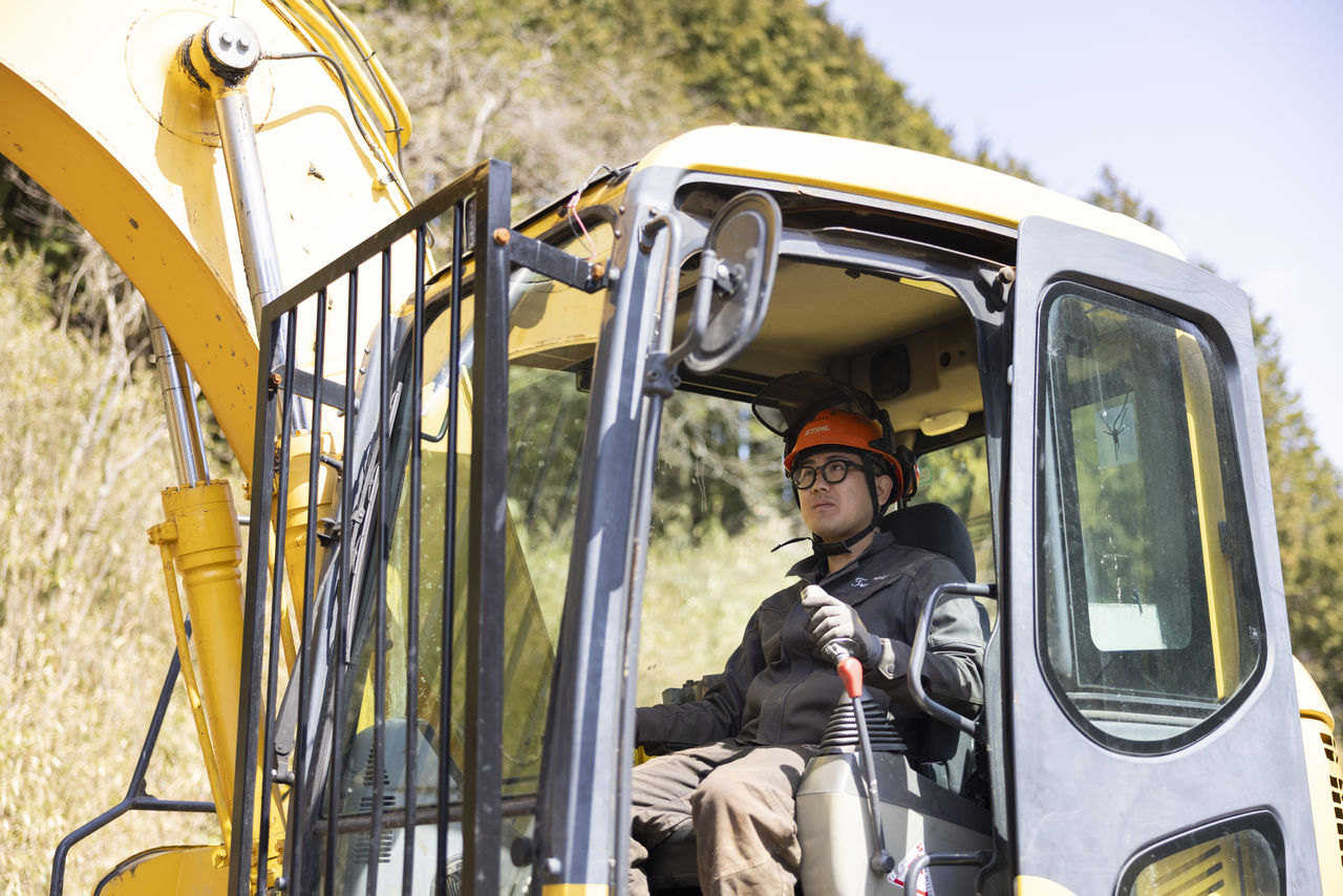 黄色い重機の運転席に座り、レバーを握って操作を行う作業員