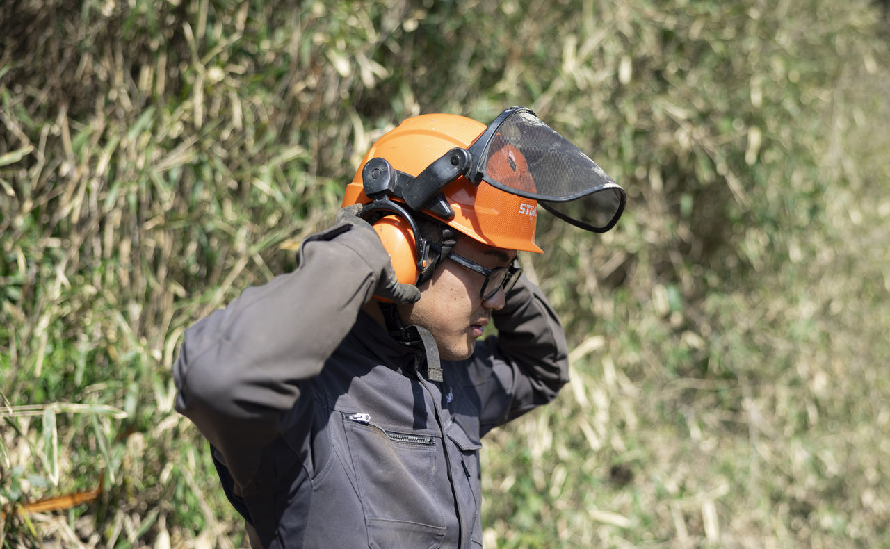 イヤーマフ付きのオレンジ色のヘルメットを被り、位置を調整する三宅さん