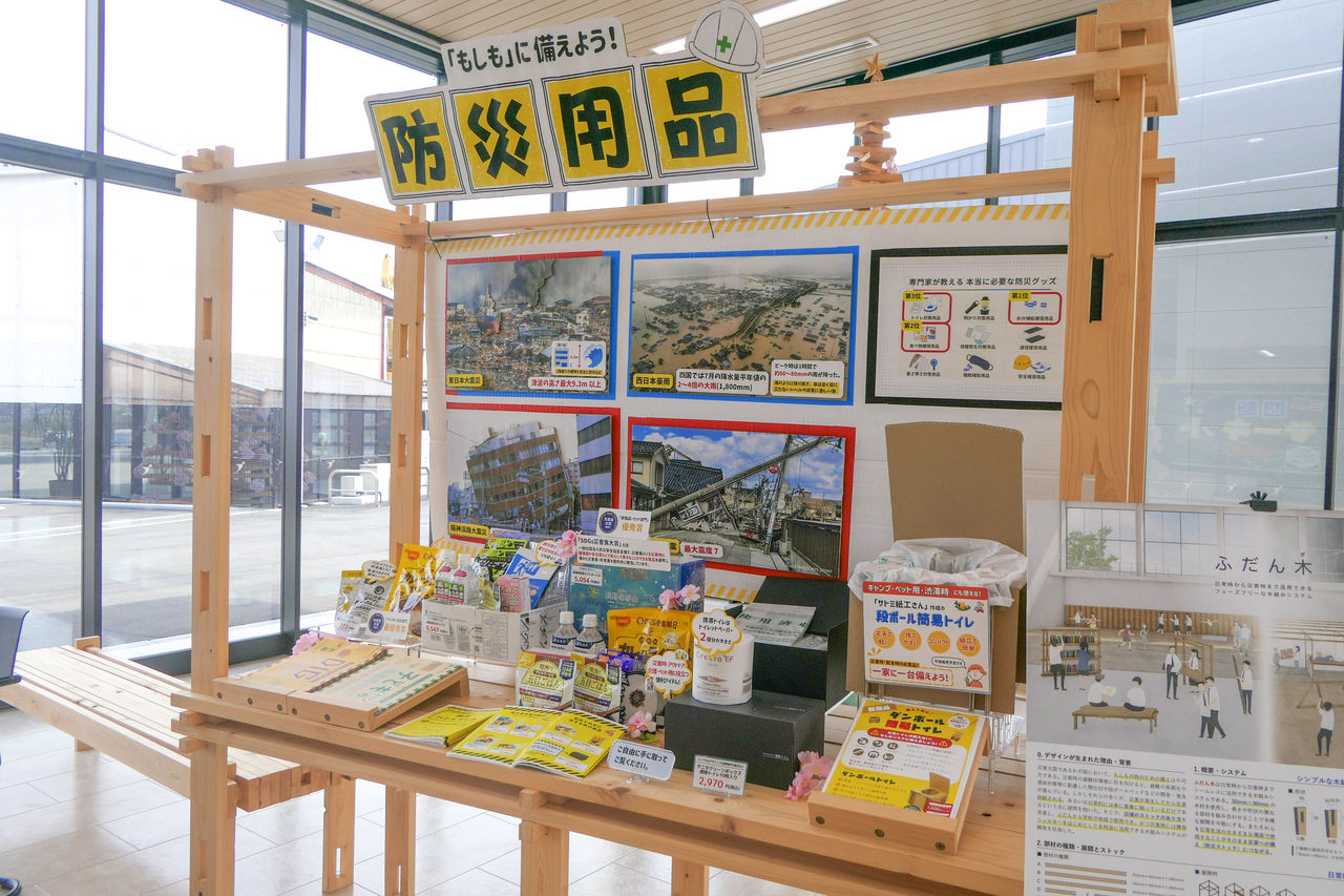 非常食、保存水、簡易トイレなどの防災グッズが木製の棚に並べられた特設展示コーナー。
