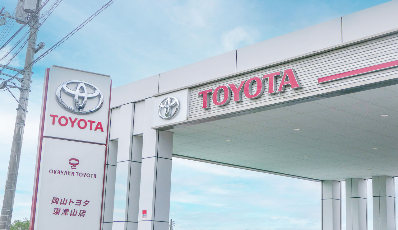青空を背景にした岡山トヨタ東津山店の外観。赤い「TOYOTA」のロゴが掲げられた白い看板と店舗入り口が見える。