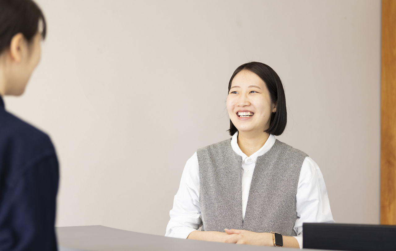 受付カウンター越しに、来店したお客様を笑顔で出迎えて対応している加藤さん。