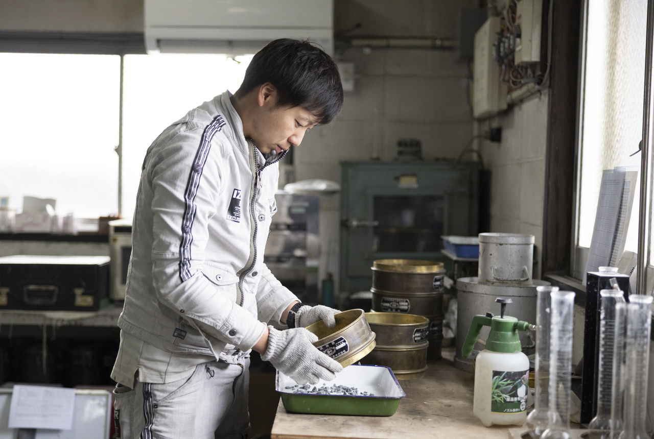 試験室の作業台で、ふるいを使って砕石の品質検査に取り組む大寺さん。