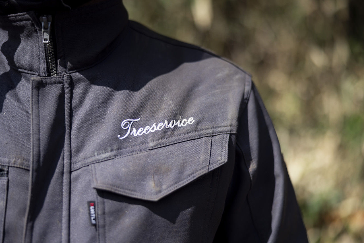 Treeserviceの白いロゴが胸元に刺繍されたグレーの作業着